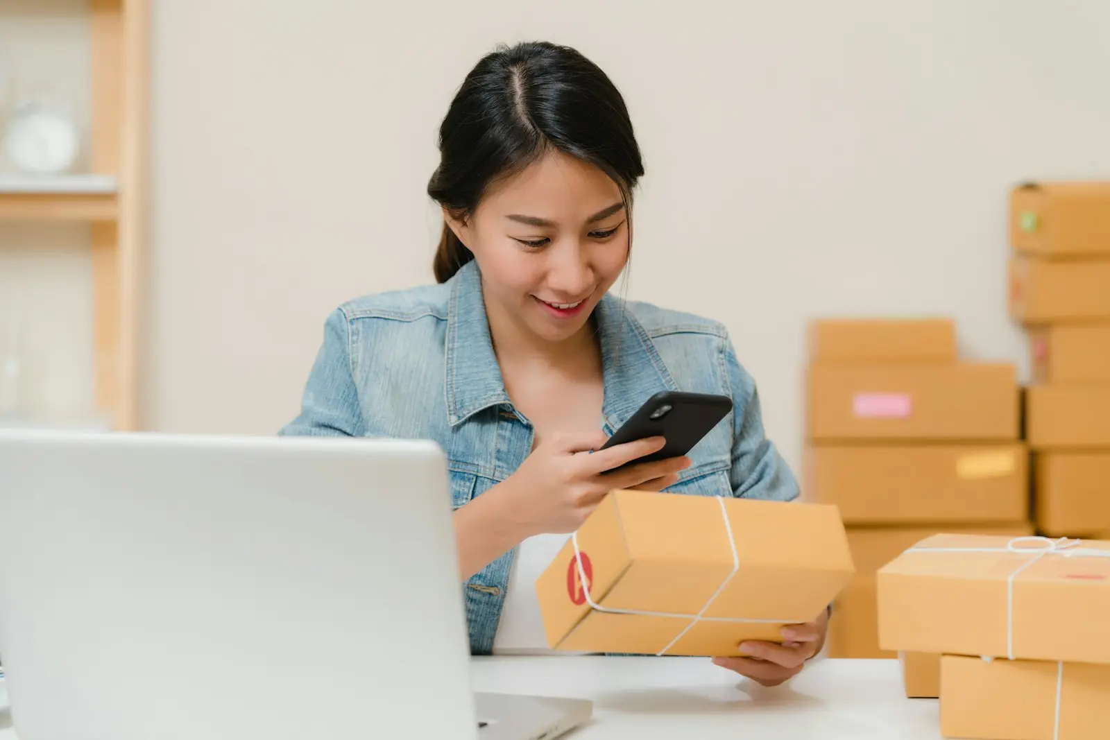 Commerçante vérifiant une commande sur son téléphone entre des colis