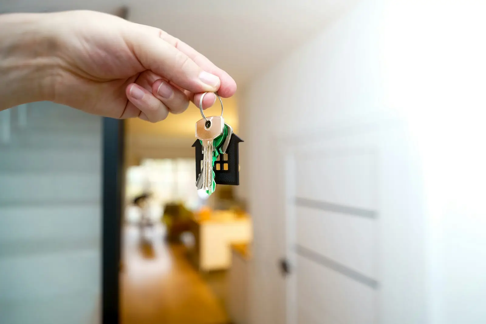 Main tendant des clés devant la porte ouverte d’un appartement lumineux
